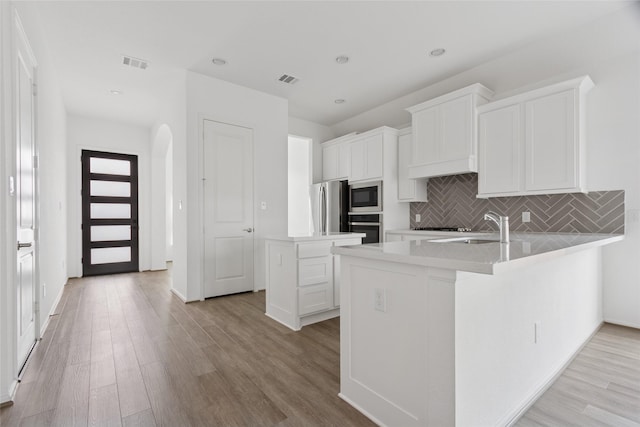 18415 Circle Bar Ranch Ct, Cypress, TX 77433 - kitchen with appliances with stainless steel finishes, light wood-type flooring, backsplash, white cabinets, and a peninsula