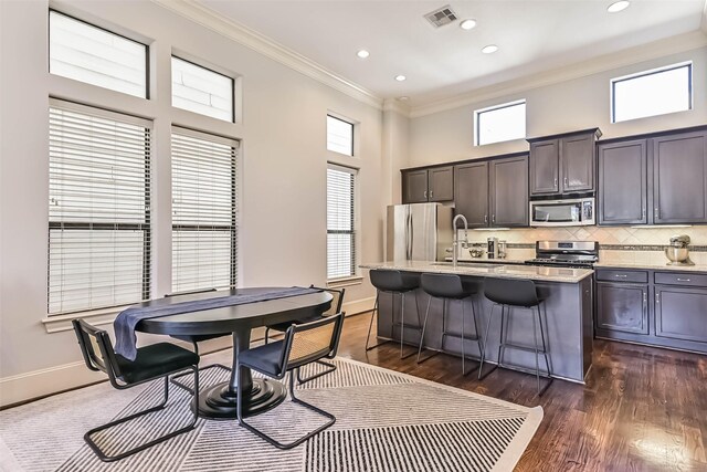 2425 Polk St, Houston, TX 77003 - kitchen featuring appliances with stainless steel finishes, a sink, crown molding, an island with sink, and dark wood finished floors