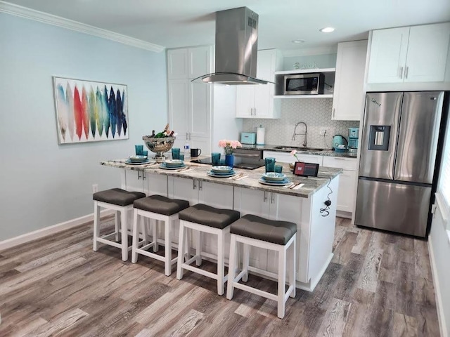 1513 47th St, Galveston, TX 77551 - kitchen featuring appliances with stainless steel finishes, island range hood, a sink, wood finished floors, and crown molding