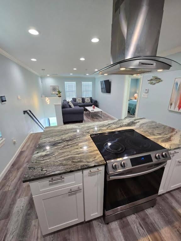 1513 47th St, Galveston, TX 77551 - kitchen featuring stainless steel electric range oven, island range hood, white cabinets, stone counters, and dark wood-style floors