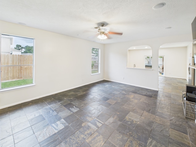 1035 Turnberry Park Ln, Spring, TX 77373 - unfurnished room featuring plenty of natural light, ceiling fan, baseboards, stone tile floors, and a textured ceiling