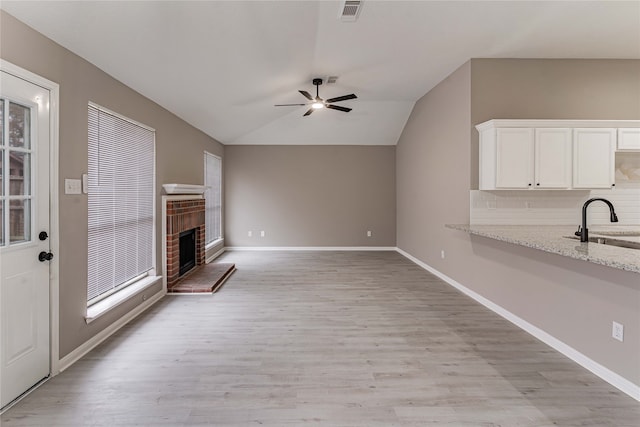 3626 Liles Ln, Humble, TX 77396 - unfurnished living room with a ceiling fan, light wood-style floors, a brick fireplace, lofted ceiling, and a sink