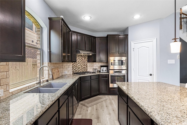 16714 Radiant Lilac Trl, Cypress, TX 77433 - kitchen featuring a sink, appliances with stainless steel finishes, light wood finished floors, under cabinet range hood, and light stone countertops