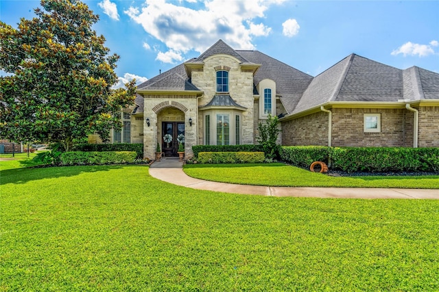 2509 Creektrail Ln, Richmond, TX 77406 - french country inspired facade with roof with shingles, a front lawn, french doors, stone siding, and brick siding