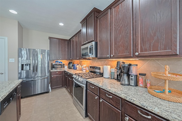 24623 Forest Hiker Ct, Katy, TX 77493 - kitchen featuring appliances with stainless steel finishes, light stone countertops, dark brown cabinetry, tasteful backsplash, and light tile patterned floors