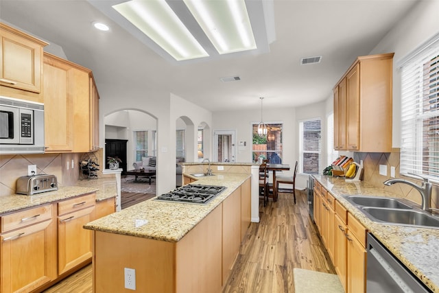 6406 Pine Reserve Dr, Spring, TX 77389 - kitchen featuring appliances with stainless steel finishes, arched walkways, light brown cabinets, a kitchen island, and light wood-style floors