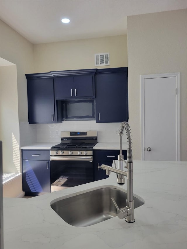 11544 Springshire Dr, Houston, TX 77066 - kitchen featuring stainless steel range with gas stovetop, black microwave, tasteful backsplash, a sink, and blue cabinets