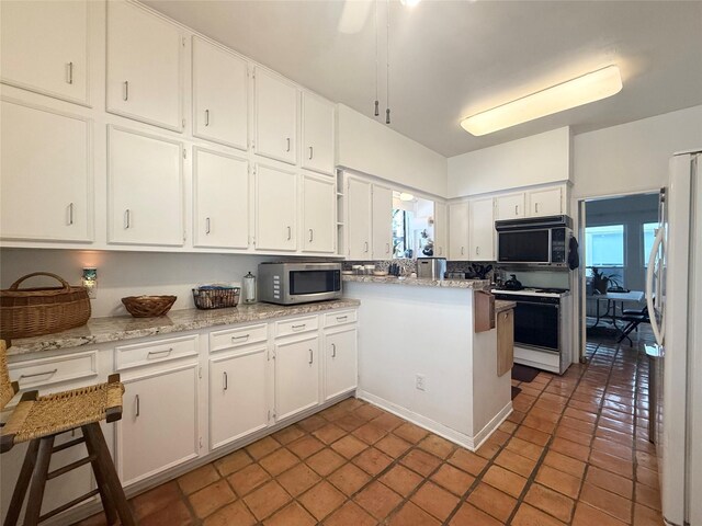 4703 Yoakum Blvd, Houston, TX 77006 - kitchen with stainless steel microwave, white gas range, freestanding refrigerator, white cabinetry, and a peninsula