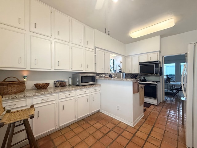 4703 Yoakum Blvd, Houston, TX 77006 - kitchen with stainless steel microwave, white gas range oven, freestanding refrigerator, white cabinetry, and a peninsula