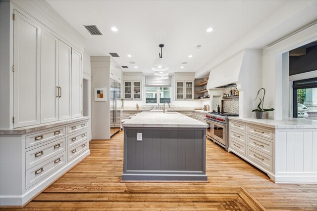 501 Avondale St, Houston, TX 77006 - kitchen featuring double oven range, white cabinets, light wood-style floors, an island with sink, and recessed lighting