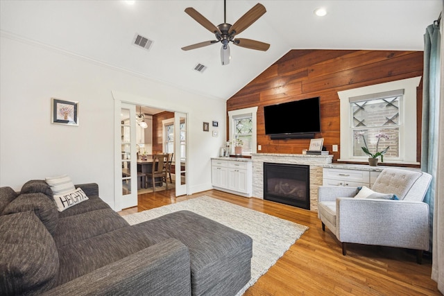 1128 W Temple St, Houston, TX 77009 - living room featuring a ceiling fan, wood walls, vaulted ceiling, light wood finished floors, and a stone fireplace