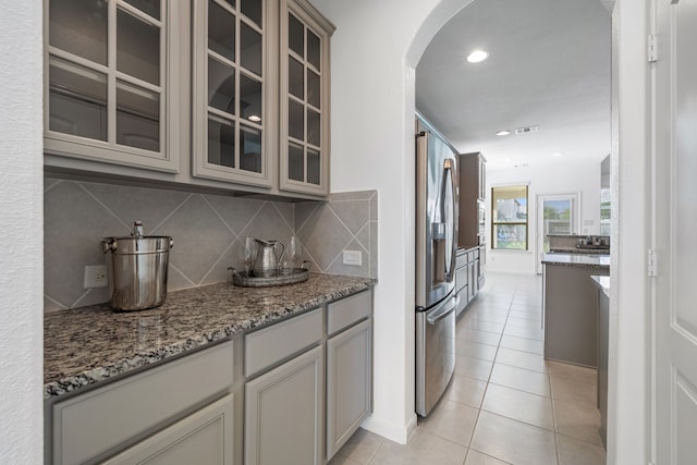 18719 Big Elm Dr, Cypress, TX 77433 - kitchen featuring stainless steel refrigerator with ice dispenser, arched walkways, tasteful backsplash, light tile patterned flooring, and light stone countertops