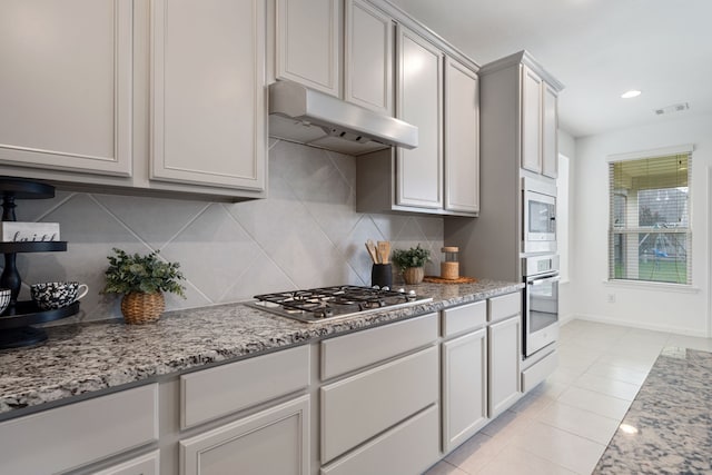 18719 Big Elm Dr, Cypress, TX 77433 - kitchen with appliances with stainless steel finishes, under cabinet range hood, tasteful backsplash, light tile patterned floors, and light stone counters