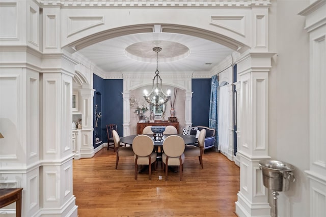 11 Hope Valley Pl, The Woodlands, TX 77382 - dining room featuring a decorative wall, ornate columns, light wood-style flooring, a chandelier, and arched walkways