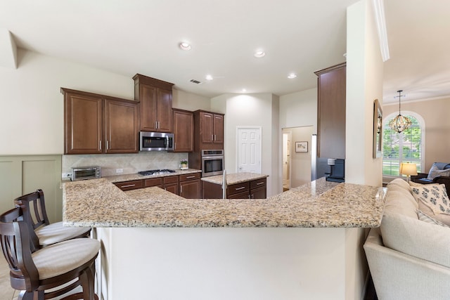 813 Woodland Ct, Conroe, TX 77302 - kitchen with stainless steel appliances, light stone counters, dark brown cabinetry, a kitchen breakfast bar, and a peninsula