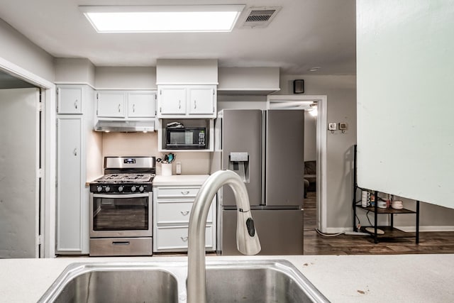 204 Carnation St, Lake Jackson, TX 77566 - kitchen with appliances with stainless steel finishes, under cabinet range hood, light countertops, dark wood-style floors, and white cabinetry