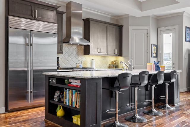 3909 Rose St, Houston, TX 77007 - kitchen with stainless steel built in fridge, wall chimney range hood, a kitchen island with sink, wood finished floors, and ornamental molding