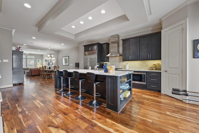 3909 Rose St, Houston, TX 77007 - kitchen featuring wall chimney range hood, built in appliances, a kitchen breakfast bar, an island with sink, and wood-type flooring