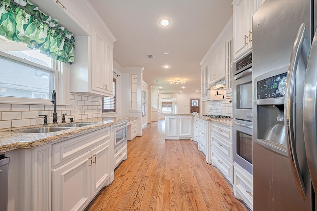 901 W 21st St, Houston, TX 77008 - kitchen with stainless steel appliances, a sink, white cabinets, backsplash, and light wood-style flooring