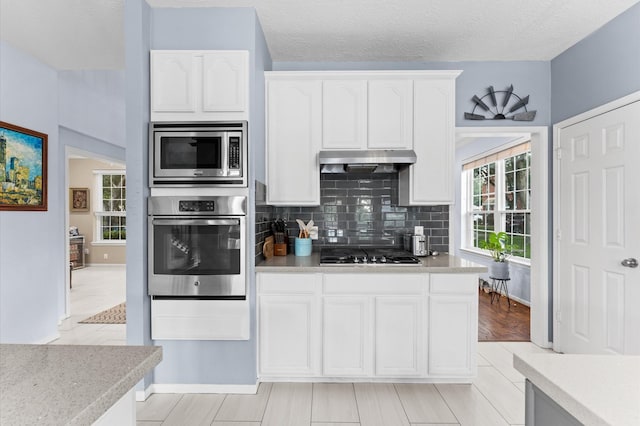 4807 Louisa Ct, Sugar Land, TX 77478 - kitchen featuring appliances with stainless steel finishes, under cabinet range hood, white cabinets, backsplash, and healthy amount of natural light