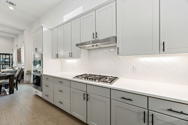 1433 Alexander St, Houston, TX 77008 - kitchen with under cabinet range hood, stainless steel appliances, light wood-type flooring, decorative backsplash, and gray cabinetry