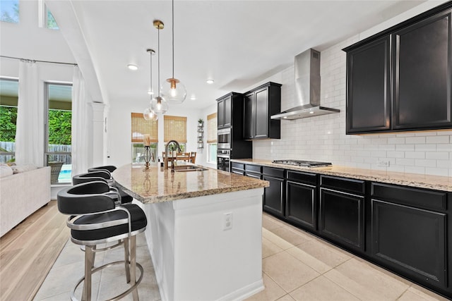399 Black Walnut Dr, Conroe, TX 77304 - kitchen with wall chimney range hood, a sink, dark cabinetry, appliances with stainless steel finishes, and light stone counters