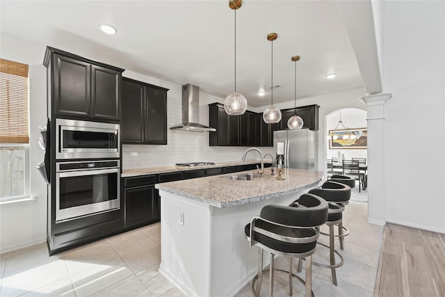 399 Black Walnut Dr, Conroe, TX 77304 - kitchen with appliances with stainless steel finishes, wall chimney exhaust hood, a sink, ornate columns, and a center island with sink