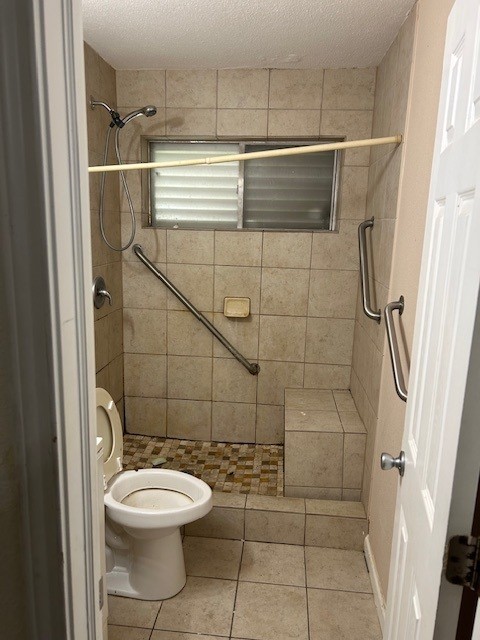 6619 Carver Ave, Hitchcock, TX 77563 - bathroom featuring toilet, a tile shower, tile patterned flooring, and a textured ceiling