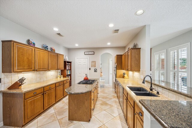 19 Remington Park, Katy, TX 77493 - kitchen featuring a sink, arched walkways, stone countertops, a kitchen island, and decorative backsplash