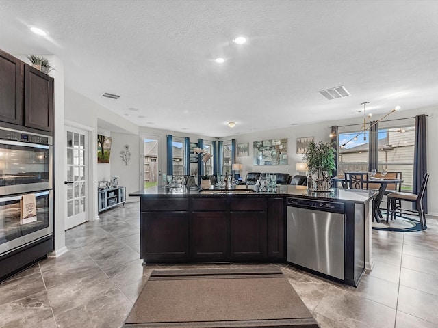 14306 Cedar Pine Ct, Houston, TX 77068 - kitchen featuring stainless steel appliances, dark countertops, dark brown cabinets, a sink, and a textured ceiling
