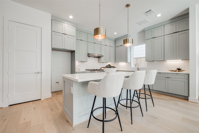 2015 Hopkins St, Houston, TX 77006 - kitchen featuring under cabinet range hood, light wood-style flooring, backsplash, gray cabinetry, and light countertops