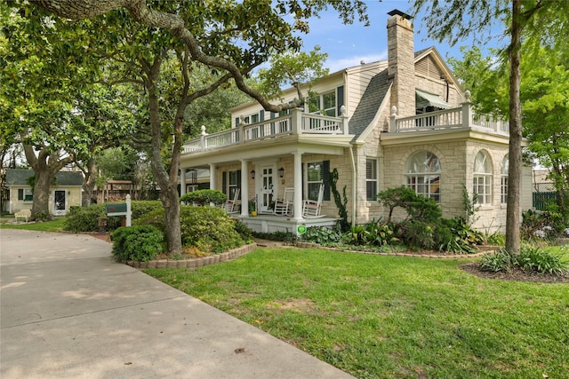 916 E James St, Baytown, TX 77520 - view of front of house with a balcony, covered porch, stone siding, a front lawn, and a chimney