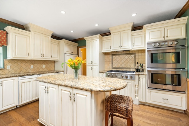 916 E James St, Baytown, TX 77520 - kitchen featuring appliances with stainless steel finishes, cream cabinetry, ornamental molding, a kitchen island, and light stone counters