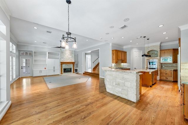 2042 Darby Ln, Fresno, TX 77545 - kitchen featuring appliances with stainless steel finishes, a stone fireplace, brown cabinetry, light wood finished floors, and a chandelier