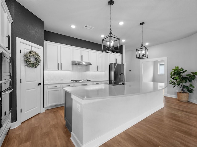 17511 Autumn Leaves Dr, Conroe, TX 77302 - kitchen featuring stainless steel appliances, under cabinet range hood, a chandelier, wood finished floors, and decorative backsplash
