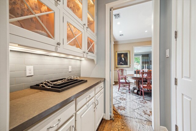 3428 Wickersham Ln, Houston, TX 77027 - kitchen featuring crown molding, white cabinets, tasteful backsplash, glass insert cabinets, and wood finished floors
