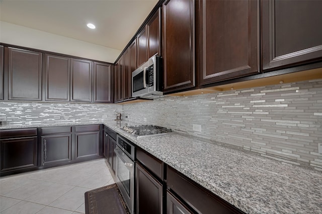 27003 Lindenwood Creek Ln, Katy, TX 77494 - kitchen with appliances with stainless steel finishes, light tile patterned flooring, tasteful backsplash, dark brown cabinetry, and light stone counters