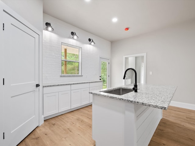 71 Prescott Dr, New Waverly, TX 77358 - kitchen featuring a sink, light wood-style flooring, white cabinetry, light stone countertops, and a center island with sink