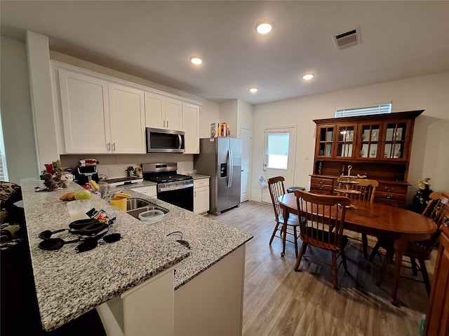 21402 Rising Fawn Rd, Porter, TX 77365 - kitchen featuring appliances with stainless steel finishes, a sink, light wood-style flooring, light stone countertops, and white cabinetry