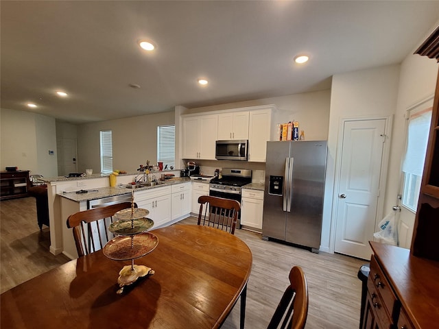 21402 Rising Fawn Rd, Porter, TX 77365 - kitchen featuring appliances with stainless steel finishes, a peninsula, light wood-type flooring, white cabinetry, and recessed lighting