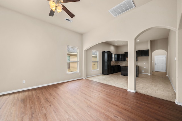 25426 Saddlebrook Champion Way, Tomball, TX 77375 - unfurnished living room with a ceiling fan, light wood-style floors, arched walkways, recessed lighting, and a high ceiling