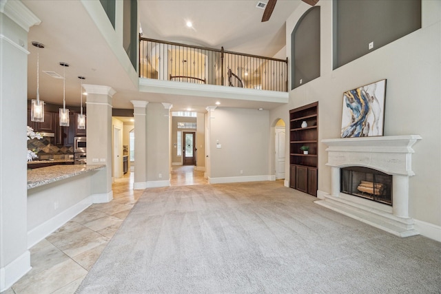 14603 Hampton Green Ln, Houston, TX 77044 - unfurnished living room featuring built in shelves, a fireplace with raised hearth, a towering ceiling, baseboards, and decorative columns