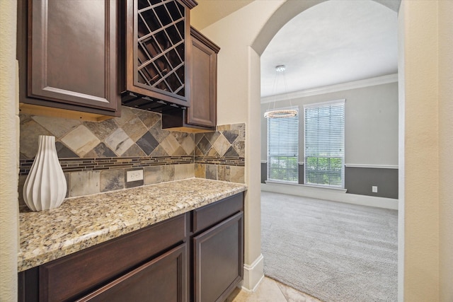14603 Hampton Green Ln, Houston, TX 77044 - kitchen with arched walkways, dark brown cabinetry, crown molding, backsplash, and light stone counters