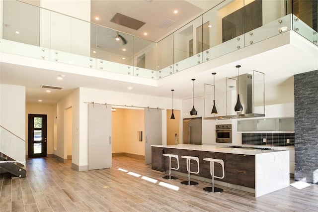 2214 Hewitt Dr, Houston, TX 77018 - kitchen featuring stainless steel appliances, island range hood, modern cabinets, a towering ceiling, and light wood-type flooring
