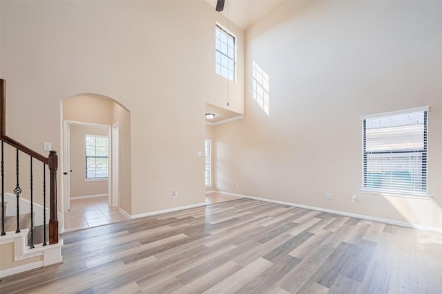 10015 Black Birch Ln, Tomball, TX 77375 - unfurnished living room featuring arched walkways, a towering ceiling, light wood-type flooring, stairway, and baseboards