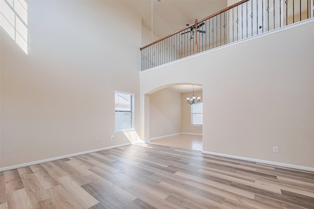 10015 Black Birch Ln, Tomball, TX 77375 - unfurnished living room with a chandelier, arched walkways, a towering ceiling, wood finished floors, and baseboards