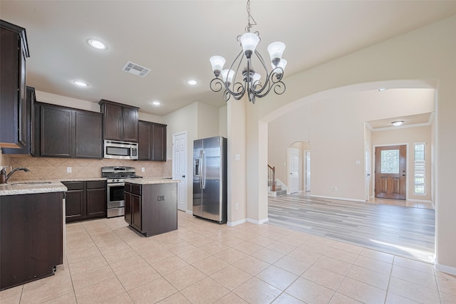 10015 Black Birch Ln, Tomball, TX 77375 - kitchen with stainless steel appliances, arched walkways, decorative backsplash, light tile patterned floors, and a center island