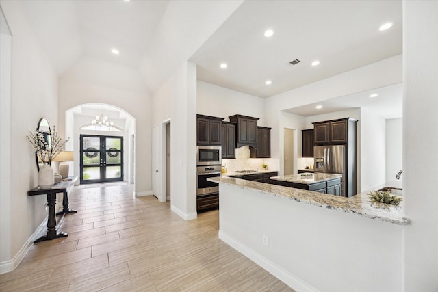 2314 Umber Oaks Ln, Brookshire, TX 77423 - kitchen featuring appliances with stainless steel finishes, a kitchen island, dark brown cabinets, light stone counters, and a chandelier