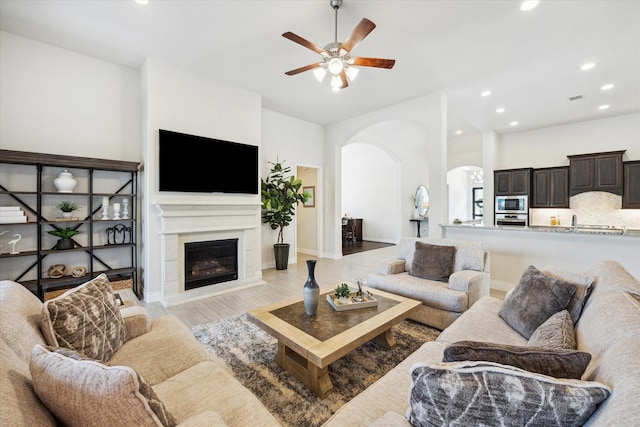 2314 Umber Oaks Ln, Brookshire, TX 77423 - living area with arched walkways, a ceiling fan, recessed lighting, a glass covered fireplace, and light wood-style floors