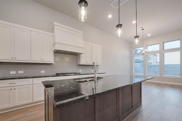 5106 Blooming Hibiscus Ln, Manvel, TX 77578 - kitchen featuring a sink, custom exhaust hood, tasteful backsplash, dark stone counters, and light wood-style floors